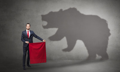 Businessman standing with red cloth in his hand and big bear shadow on his background
