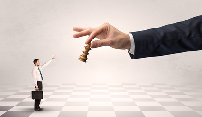 Small businessman fighting against big chessman on a big hand with chess board concept
