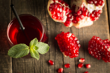Pomegranate juice with fresh pomegranate fruits on wooden background. soft drink with lime, mint and ice.