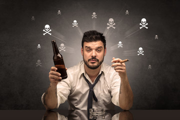 Loser drunk man sitting at table with skulls concept around

