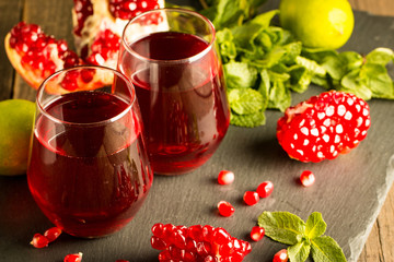 Pomegranate juice with fresh pomegranate fruits on wooden background. soft drink with lime, mint and ice.