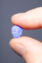 Fingers holding a blue MDMA, Amphetamine, Army Skull, Ecstasy, XTC pill on a grey background.