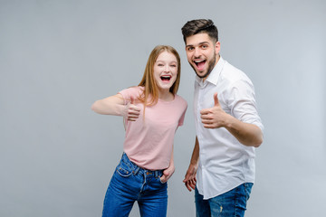 Happy young couple of man and woman showing thumbs up isolated over grey background