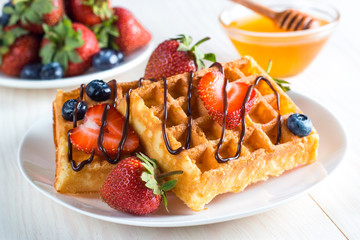 Fresh homemade food of berry Belgian waffles with honey, chocolate, strawberry, blueberry, maple syrup and cream. Healthy dessert breakfast concept with juice