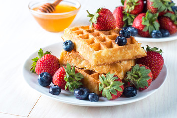 Fresh homemade food of berry Belgian waffles with honey, chocolate, strawberry, blueberry, maple syrup and cream. Healthy dessert breakfast concept with juice
