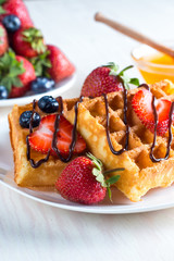 Fresh homemade food of berry Belgian waffles with honey, chocolate, strawberry, blueberry, maple syrup and cream. Healthy dessert breakfast concept with juice