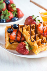 Fresh homemade food of berry Belgian waffles with honey, chocolate, strawberry, blueberry, maple syrup and cream. Healthy dessert breakfast concept with juice