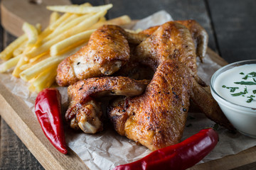 Barbecue grilled chicken wings close up with fries, tomato ketchup sauce and beer on wooden background. Meat food concept. 