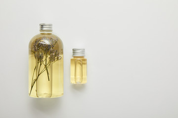 top view of transparent bottles with natural liquid yellow beauty products with herbs on grey background