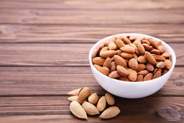 White bowl of almonds on brown wooden background