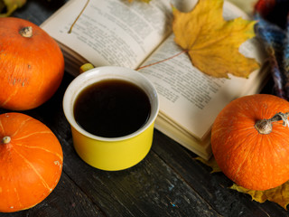 Yellow coffee Cup and old book on wooden background with autumn leaves and pumpkins