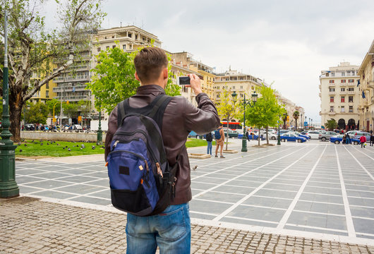 Young tourist with backpack taking pictures of a square Archeas Agoras and a pedestrian street on a smartphone in Thessaloniki, Greece