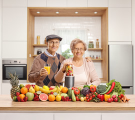 Elderly husband and wife with a pile of fruits and vegetables and a blender