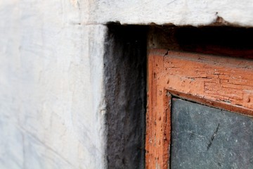 An old window in a red frame with dirty glass on a gray facade. The view is close.