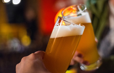Close-up view of a two glass of beer in hand. Beer glasses clinking in bar or pub