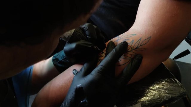Girl tattoo artist tattooing skull with flowers on male arm. Artist in front