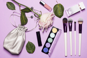 Beauty brushes with palette, beautiful pink rose, green leafs, stylish cosmetic bag of silver color on the georgios purple fon and space for text