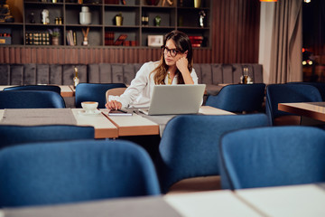 Bored businesswoman looking away while sitting in coffee shop. On desk laptop and agenda.