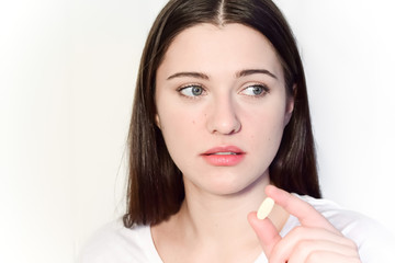 A girl is holding a pill in front of her. The young woman looks thoughtfully. Concept: health, vitamins, nutritional supplements.