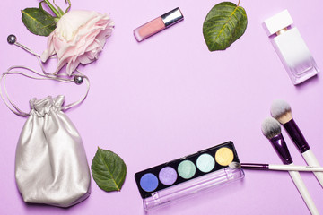 Beauty brushes with palette, beautiful pink rose, green leafs, stylish cosmetic bag of silver color on the georgios purple fon and space for text