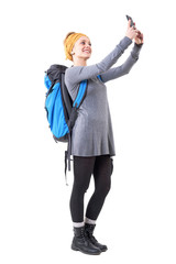 Relaxed happy traveling young woman with rucksack taking selfie with smartphone. Full body isolated on white background. 