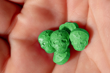 Close-up of a caucasian handpalm with green MDMA, Amphetamine, Army Skull, Ecstasy or XTC pills.