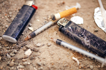 Used syringe on the ground - drugs Addiction equipment. Heroin, syringe, cigarette and lighter -...