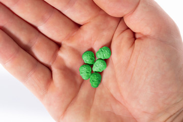 Top view of a caucasian hand with green MDMA, Amphetamine, Army Skull, Ecstasy or XTC pills on a white background..