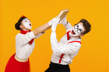 portrait of mime couple artist quarreling and reading book isolated on yellow background