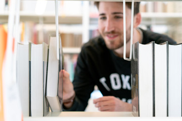 Young attractive green-eyed student smiling happily taking a book seen from the library shelf
