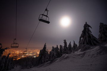 A ski lift in the night. Moon shinig over an empty ski lift. Lightrails from a headtorch and from...