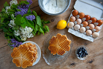 Homemade waffles with aronia, eggs and lilac flowers on the wooden table