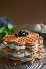 Homemade waffles with aronia, eggs and lilac flowers on the wooden table