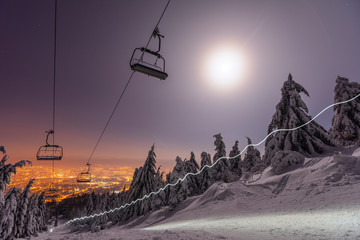 A ski lift in the night. Moon shinig over an empty ski lift. Lightrails from a headtorch and from...