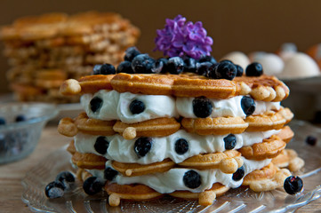 Homemade waffles with aronia, eggs and lilac flowers on the wooden table