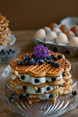 Homemade waffles with aronia, eggs and lilac flowers on the wooden table