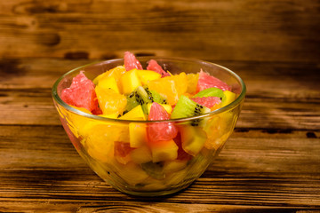 Salad with mango, oranges, grapefruit and kiwi fruits in a glass bowl on wooden table