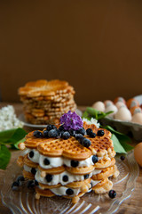Homemade waffles with aronia, eggs and lilac flowers on the wooden table