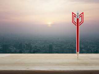 Red pencil in the shape of a dart on wooden table over aerial view of cityscape at sunset, vintage style, Business strategy concept