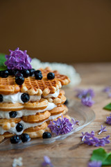 Homemade waffles with aronia, eggs and lilac flowers on the wooden table