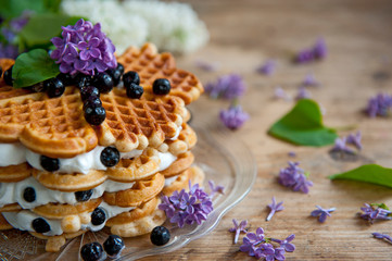 Homemade waffles with aronia, eggs and lilac flowers on the wooden table