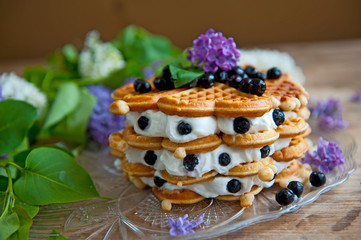 Homemade waffles with aronia, eggs and lilac flowers on the wooden table