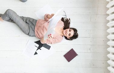 A beautiful woman lies on the floor among papers and documents, the girl freelancer smiles and relaxes during a break from work