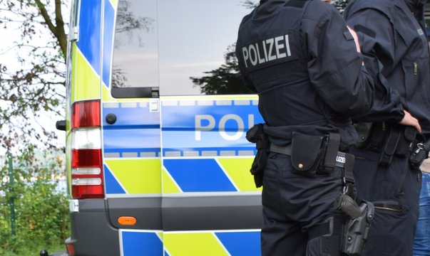 Bewaffnete Polizisten in schwarzer Uniform vor einem Polizeiauto
