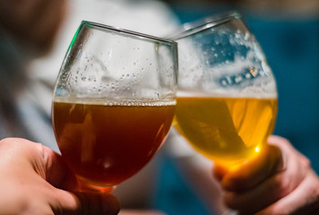 Close-up view of a two glass of beer in hand. Beer glasses clinking in bar or pub