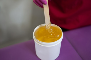 The girl collects sugar paste from white cans on a wooden stick for further sugar depilation