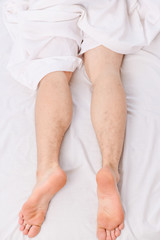 Lazy man happy waking up in the bed rising hands in the morning with fresh feeling relaxed. Handsome man using clock in bed after waking up. To wake up in the morning.