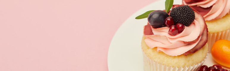 panoramic shot of cupcakes with fruits and berries on plate isolated on pink