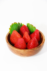 red strawberries and green leaves in a brown wooden plate on a white background