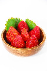 red strawberries and green leaves in a brown wooden plate on a white background